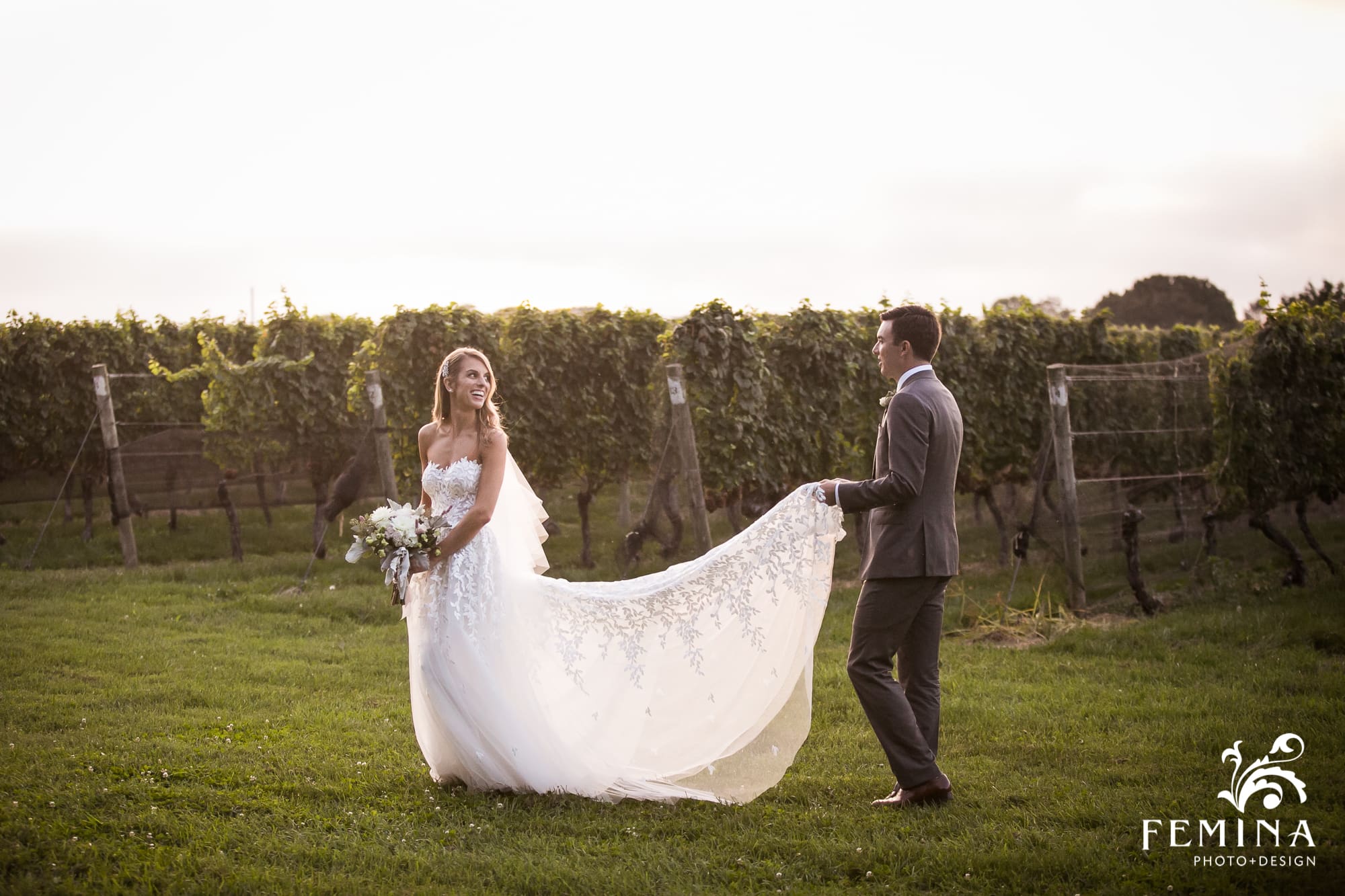Tommy carries Lindsey's dress as they walk through the vineyard at Bedell Cellars