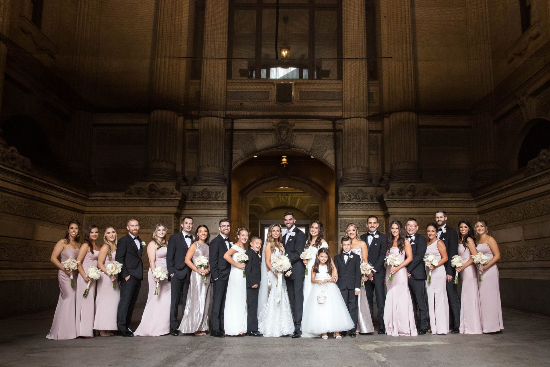 Bride and groom and their wedding party posing under City Hall in Philadelphia