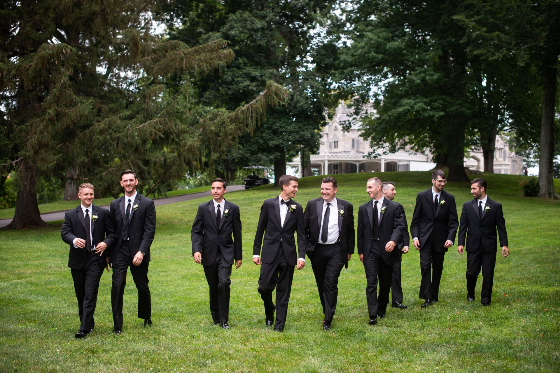Groomsmen walking and laughing on the green lawn in front of Lyndhurst Castle