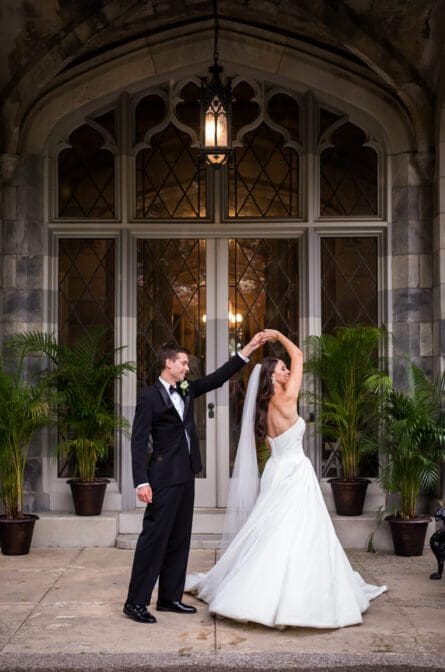 A groom is twirling the bride in front of an arched window at the historic Lyndhurst Castle