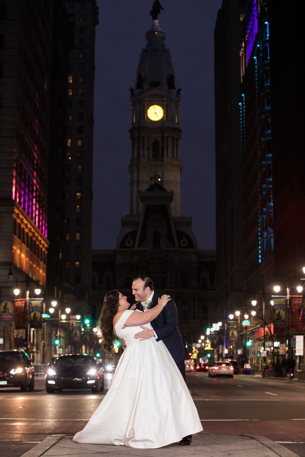 A groom holding a bride in the middle of the street on Broad Street in front of City Hall in Philadelphia
