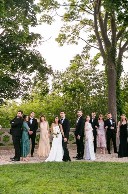 A wedding party with untraditional and mixed attire are standing in varying poses in the garden at Hempstead House