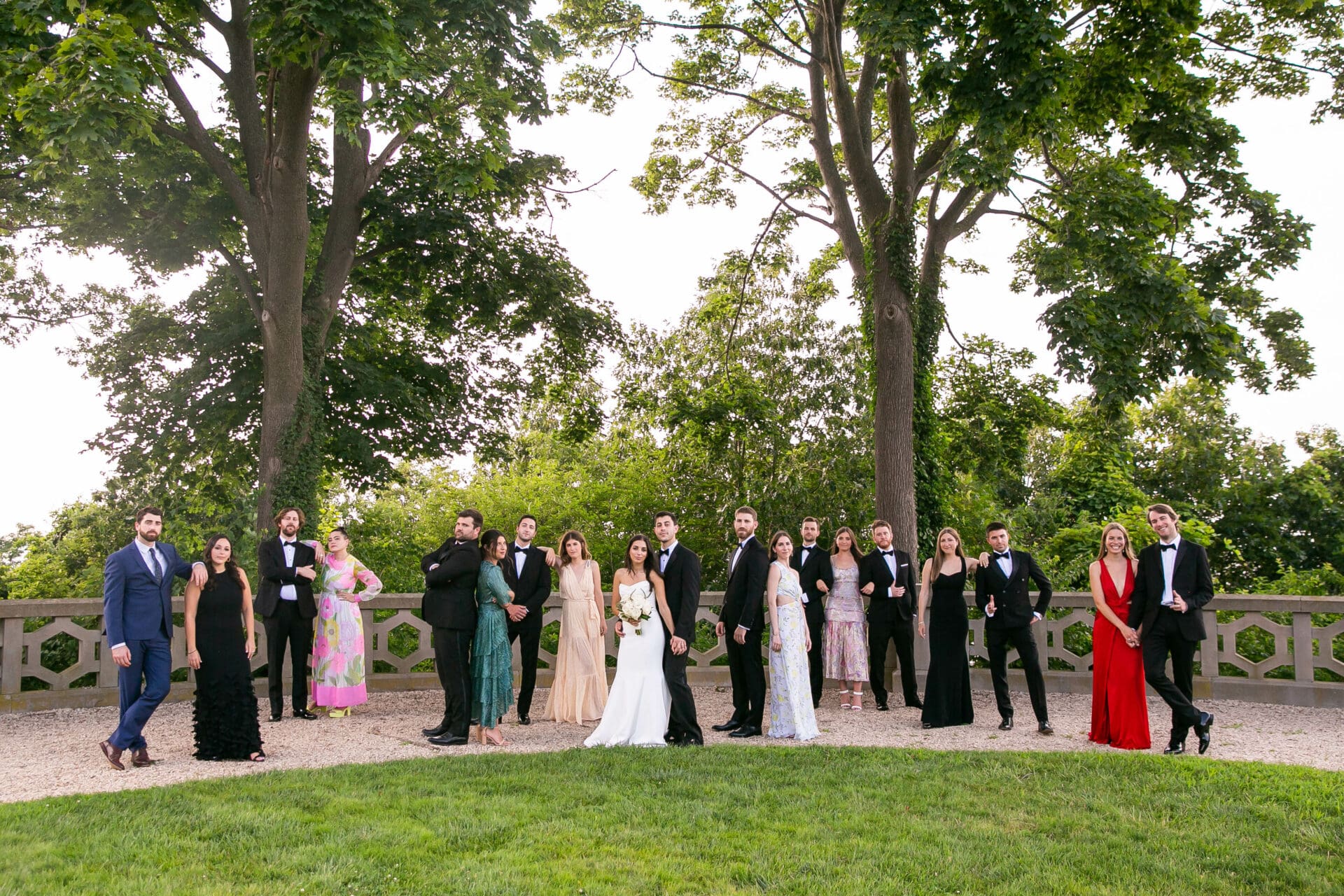 A wedding party with untraditional and mixed attire are standing in varying poses in the garden at Hempstead House