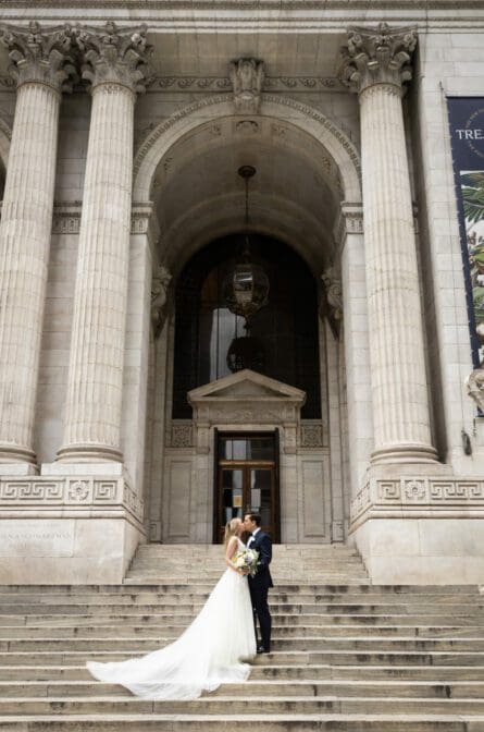 A bride and groom are kissing on the steps of the NYPL in New York City