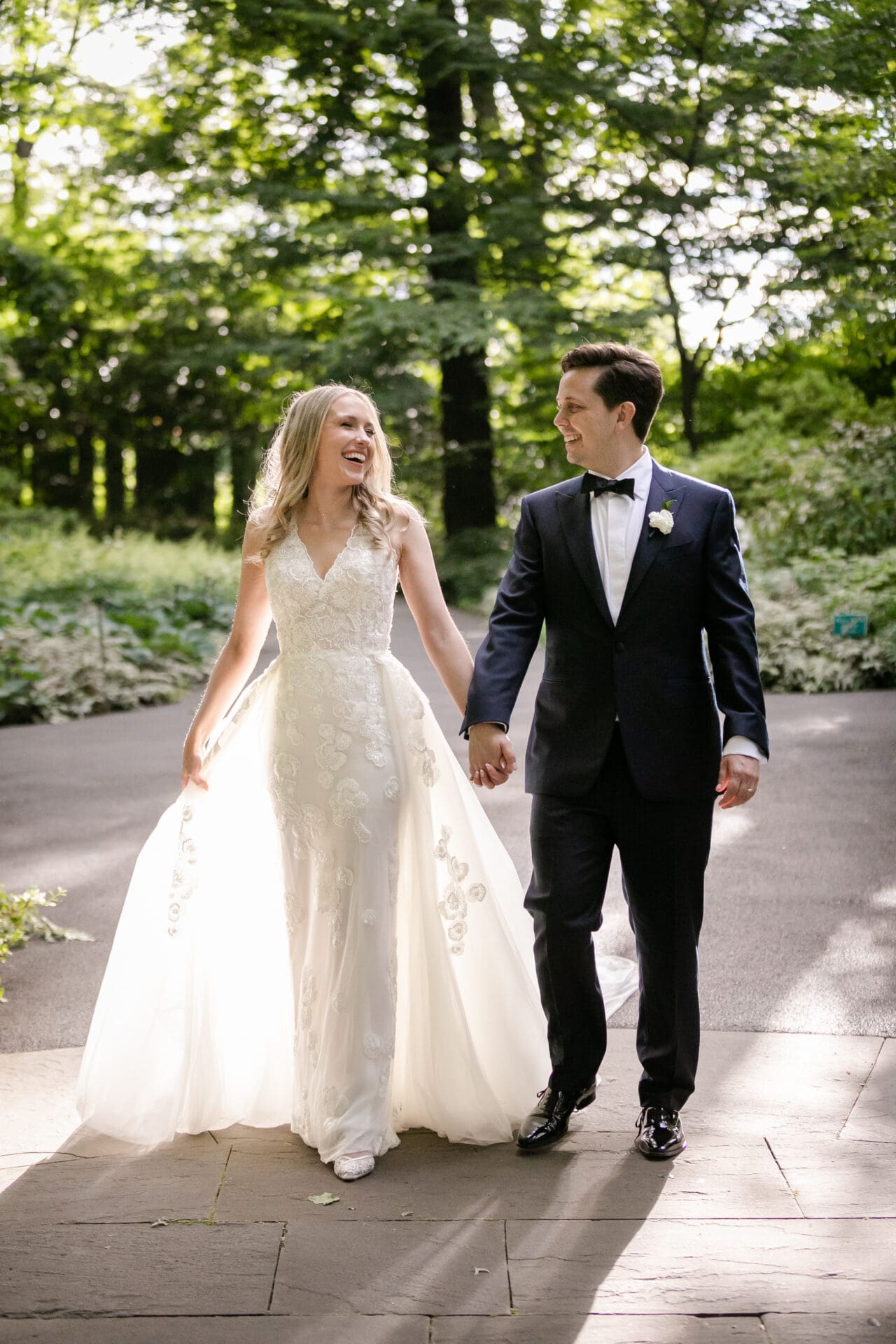 A bride and groom walking and laughing during their portrait session at the New York Botanical Garden in NY