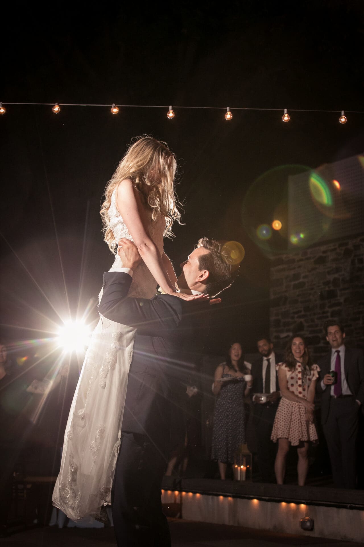 A groom lifts the bride in the air during their first dance at a night reception at the NYBG Stone Mill 