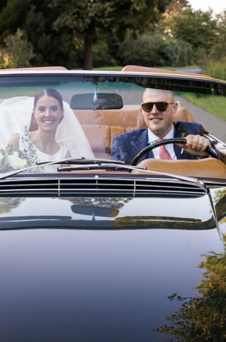 Bride and groom driving in a convertible car through the New York Botanical Gardens in NYC