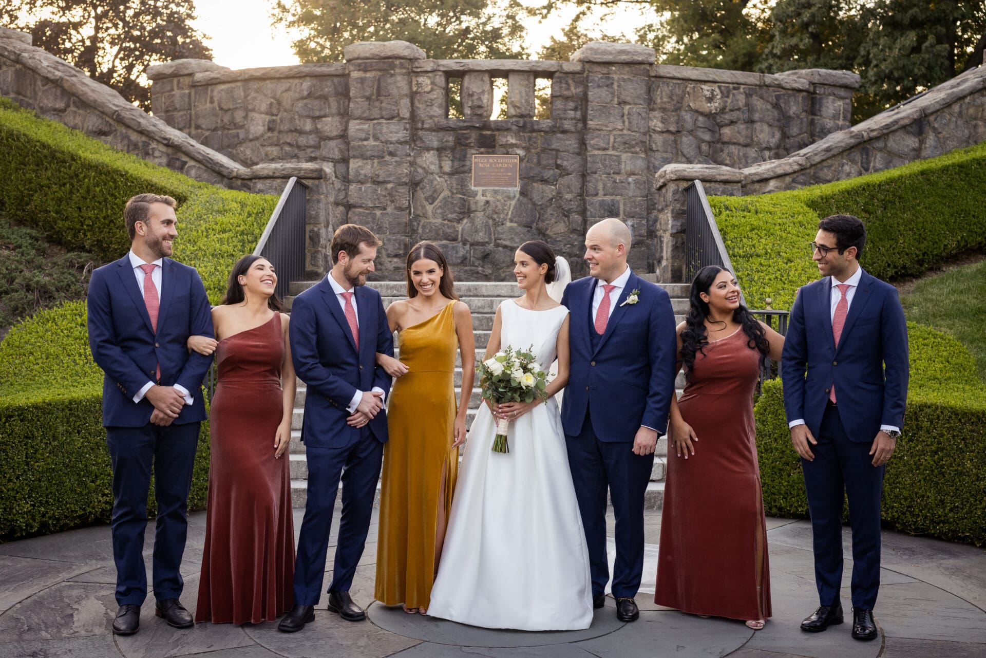 A wedding party poses in front of the stairs in the Rose Garden at the New York Botanical Gardens in the Bronx NY
